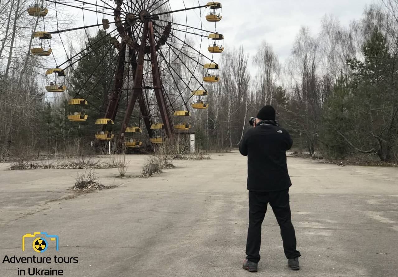 a man taking a photo of a ferris wheel in prypiat ghosttown in the chernobyl exclusion zone